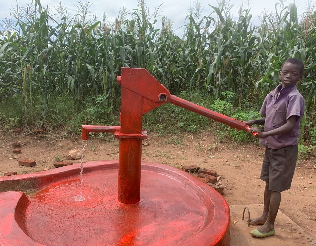 Boy using a community water pump provided by Our Aim Foundation